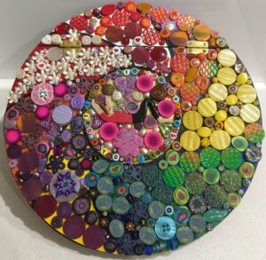 Image of a round mosaic book cover featuring polymer clay pieces and found objects.